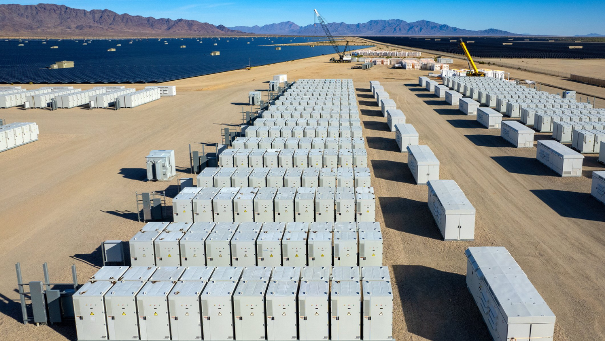 Energy storage containers lined up near a solar farm in a desert landscape.